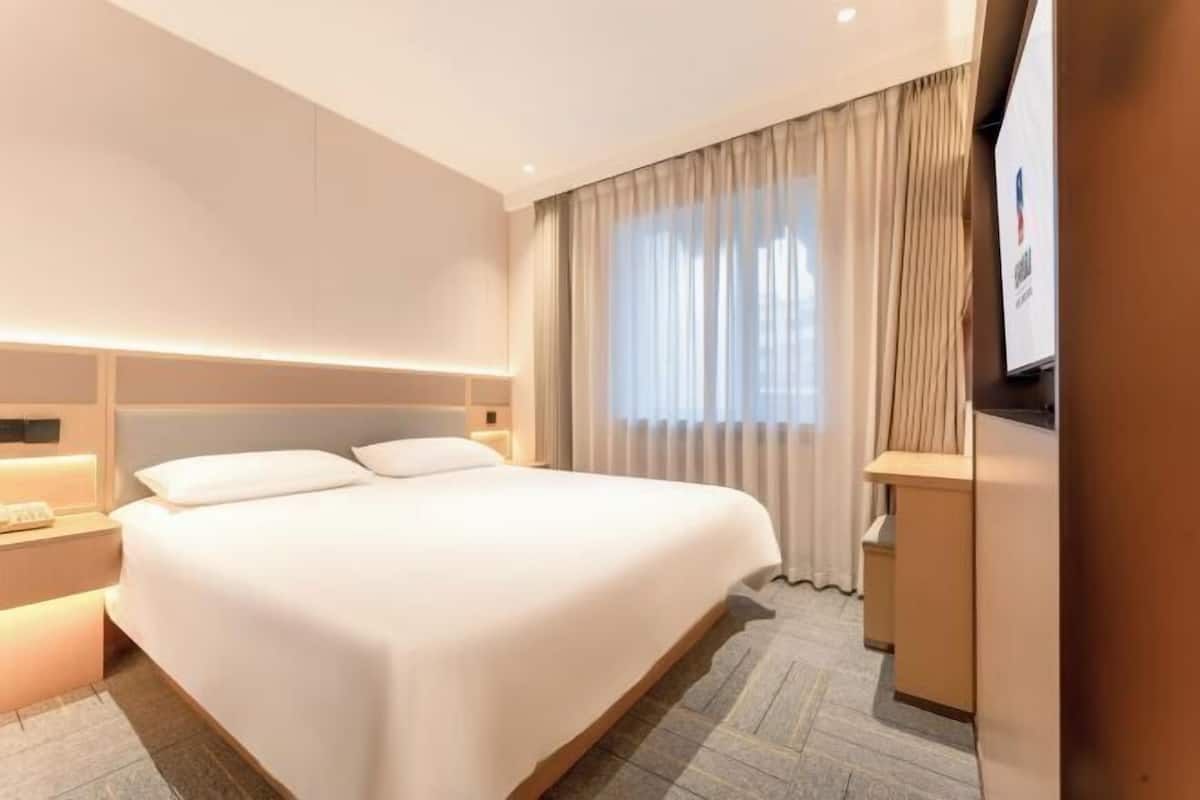 Ein Hotelzimmer mit einem großen Bett, Nachttischen, einem Schreibtisch und einem Fernseher.