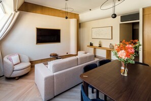 A modern living room with a sofa set, a dining table, and a TV mounted on the wall.