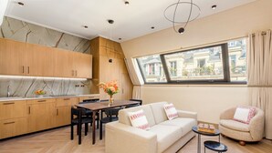 Une cuisine moderne avec des meubles en bois, un pare-feu en marbre et un coin repas comprenant une table et des chaises. On y trouve également un canapé et un fauteuil, offrant une vue sur la ville grâce à une grande fenêtre.