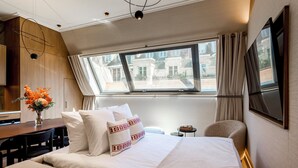 Une chambre d’hôtel avec un grand lit, un bureau, une chaise, une petite table et une fenêtre avec des rideaux.