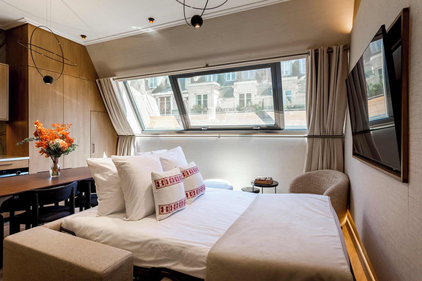 Ein Hotelzimmer mit einem großen Bett, einem Schreibtisch, einem Stuhl, einem kleinen Tisch und einem Fenster mit Vorhängen.