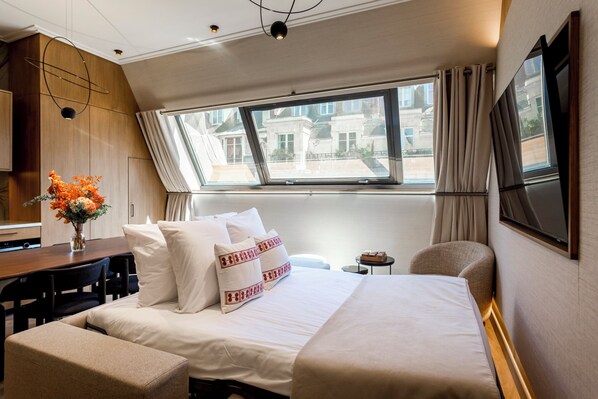 A hotel room with a large bed, a desk, a chair, a small table, and a window with curtains.