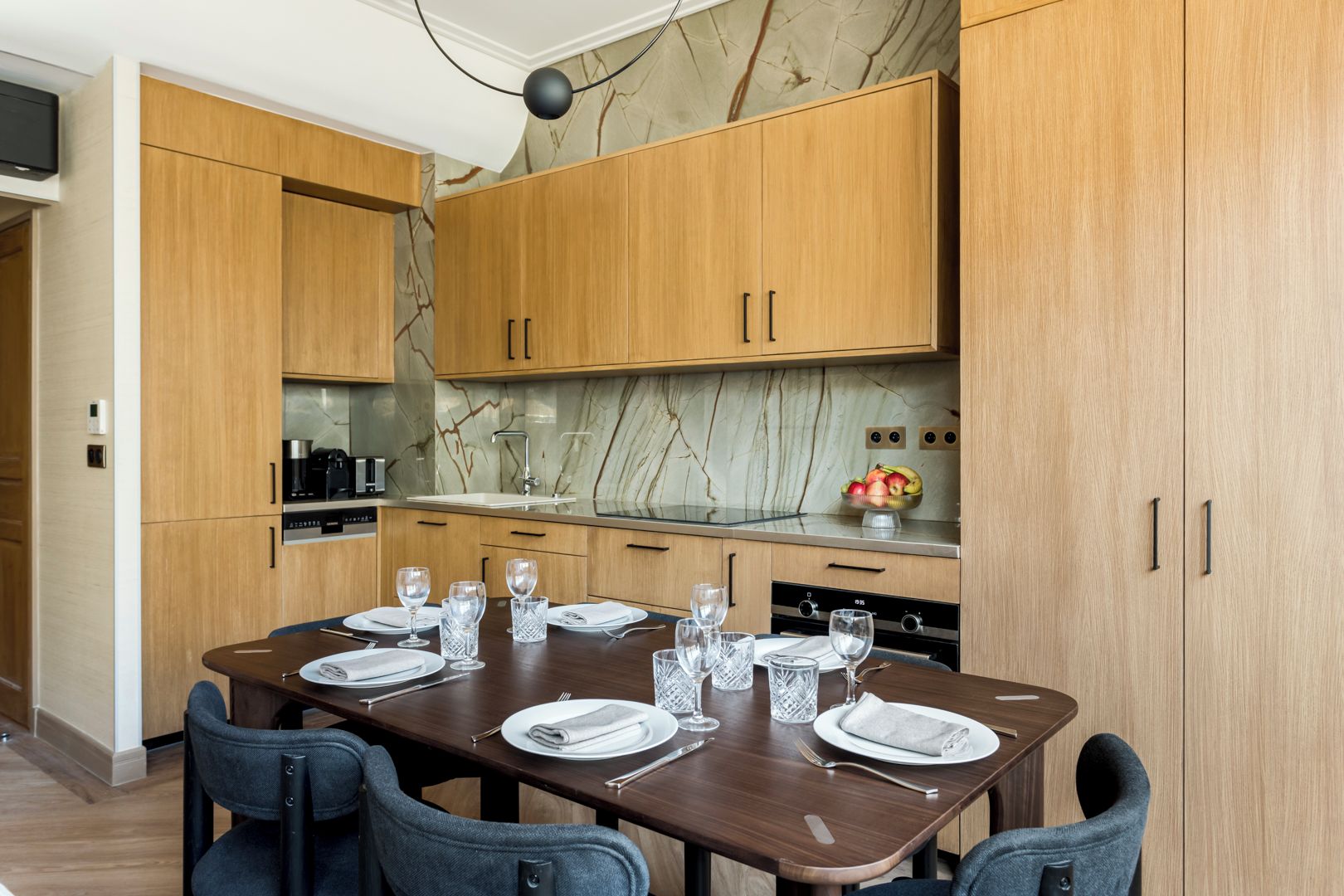 A modern kitchen with wooden cabinets, a marble backsplash, and a dining area set for six with a wooden table and chairs.