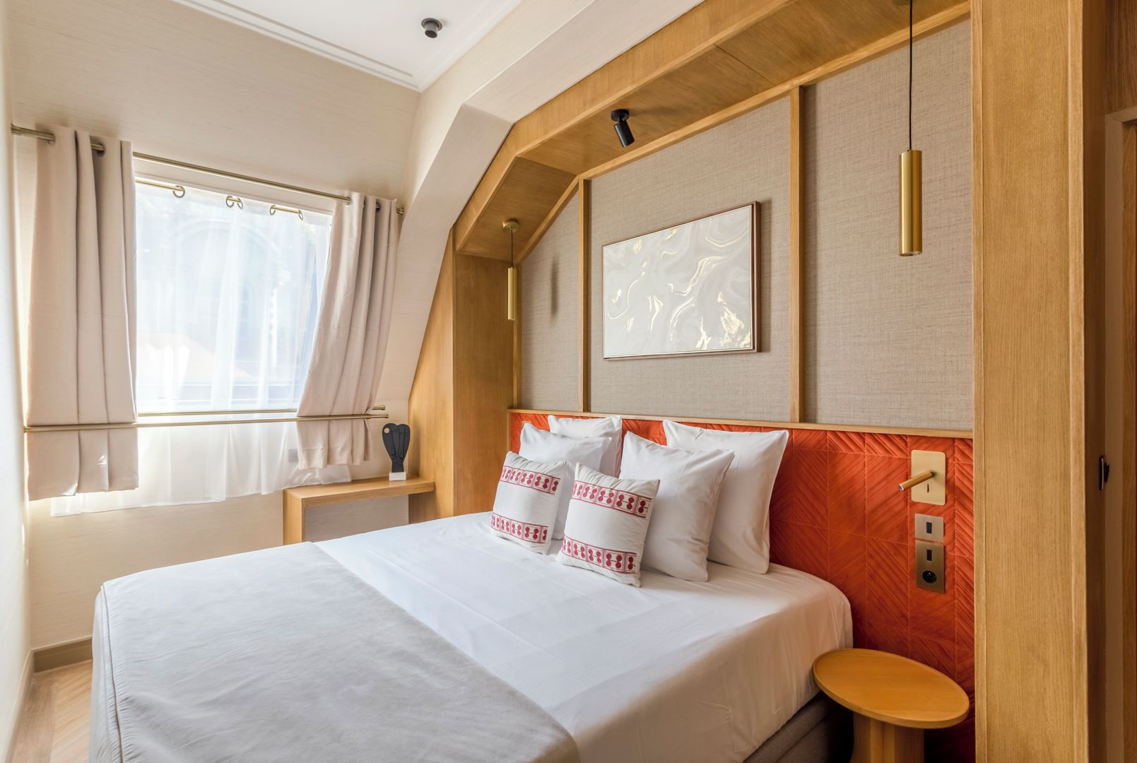 Ein Hotelzimmer mit einem großen Bett, einem Nachttisch, einem Fenster mit Vorhängen und einer Wandleuchte.