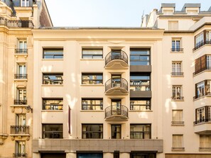 A multi-story building with a central balcony, large windows, and a flag.