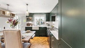 A modern kitchen with dark cabinets, a wooden herringbone floor, and pendant lighting. - Gorgeous 3 Bed, 225 Year Old Cottage (Portishead)