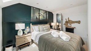 A modern bedroom with a large bed, bedside lamps, a nightstand, a radiator, and a wall-mounted artwork of a deer. - Gorgeous 3 Bed, 225 Year Old Cottage (Portishead)