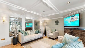 Ein modernes Wohnzimmer mit einer Couch, Sesseln, einem Couchtisch und einem Fernseher. Ein Kamin und eine Uhr sind an der Wand angebracht.