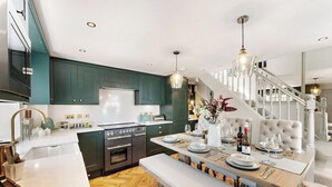 A modern kitchen with dark green cabinets, stainless steel appliances, and a wooden dining table set for four. - Gorgeous 3 Bed, 225 Year Old Cottage (Portishead)