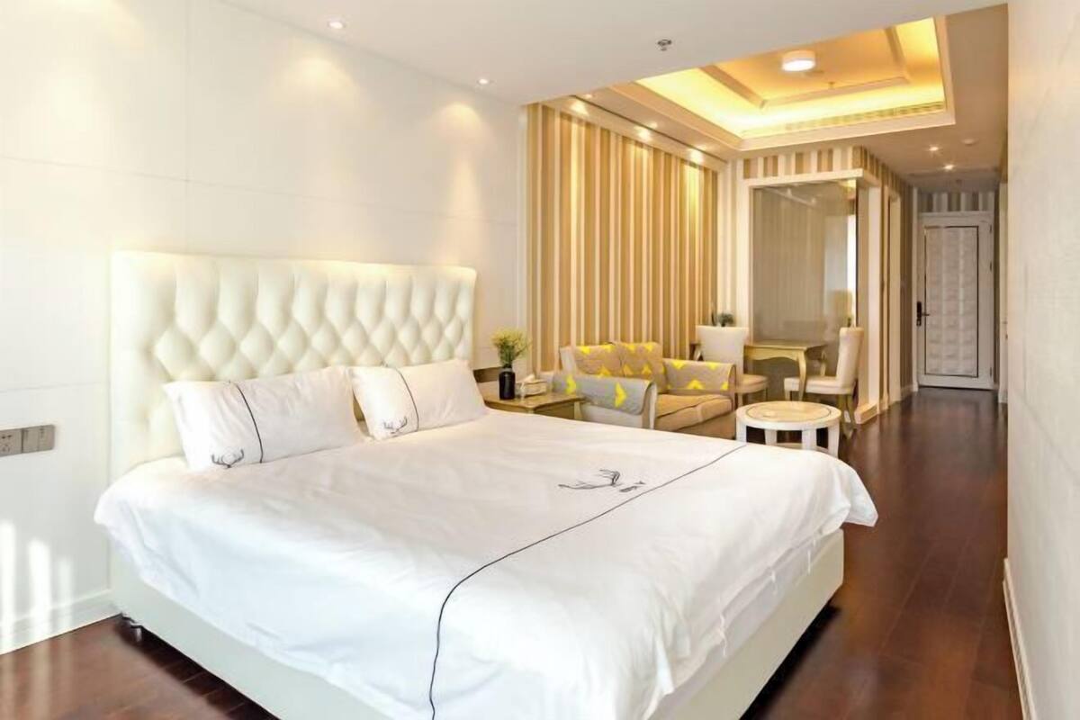 Una habitación de hotel moderna con una cama grande, un espacio de descanso con sofá y sillones, una mesita redonda y un espejo.