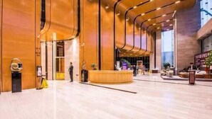 A spacious lobby with a curved reception desk, a man standing near the entrance, and a few people in the background. - Xiamen IMAY Designer Seaview Apartment (Shimao Twin Towers Branch) (Xiamen)