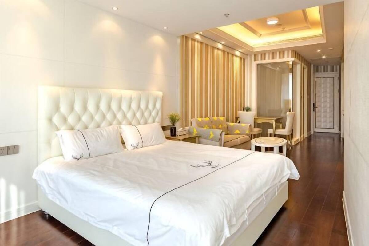 Una habitación de hotel moderna con una cama grande, un área de descanso con sofá y sillones, una mesita redonda y un espejo.