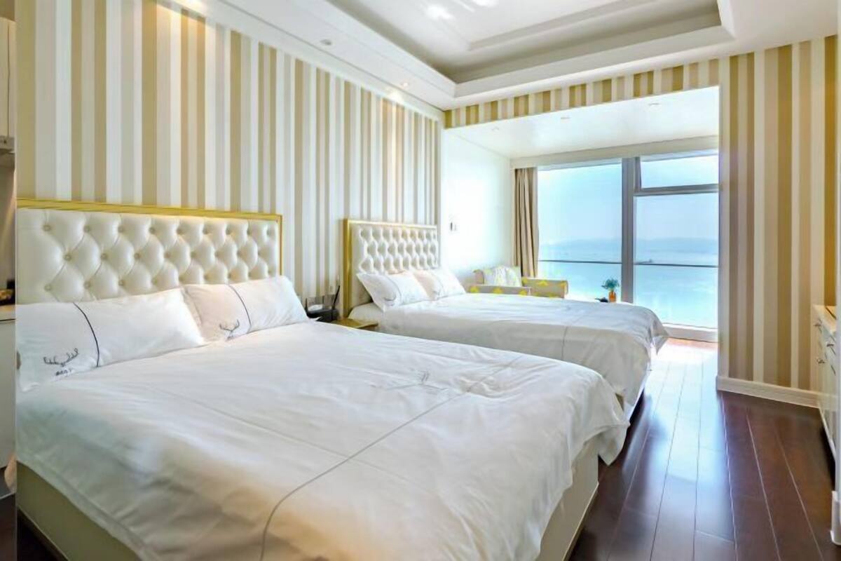 Habitación de hotel con dos camas, papel tapiz a rayas y un ventanal con vista al mar.