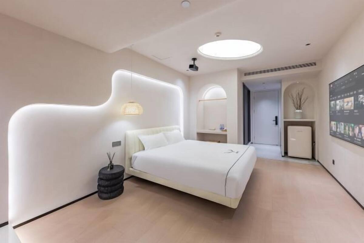 Un dormitorio moderno con cama, mesita de noche, lámpara y televisor montado en la pared.
