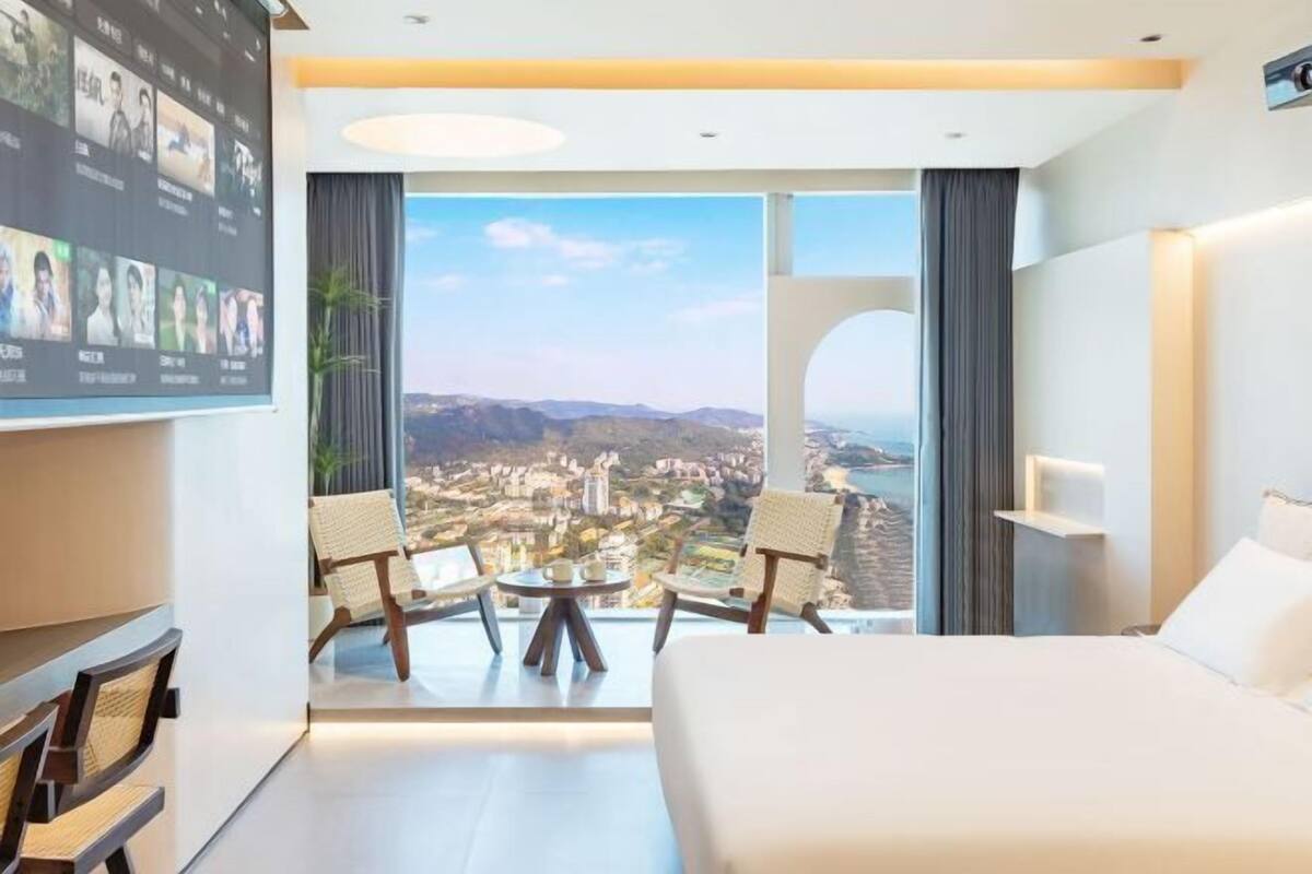 Habitación de hotel con una cama grande, un televisor montado en la pared y un balcón con vista a la ciudad.