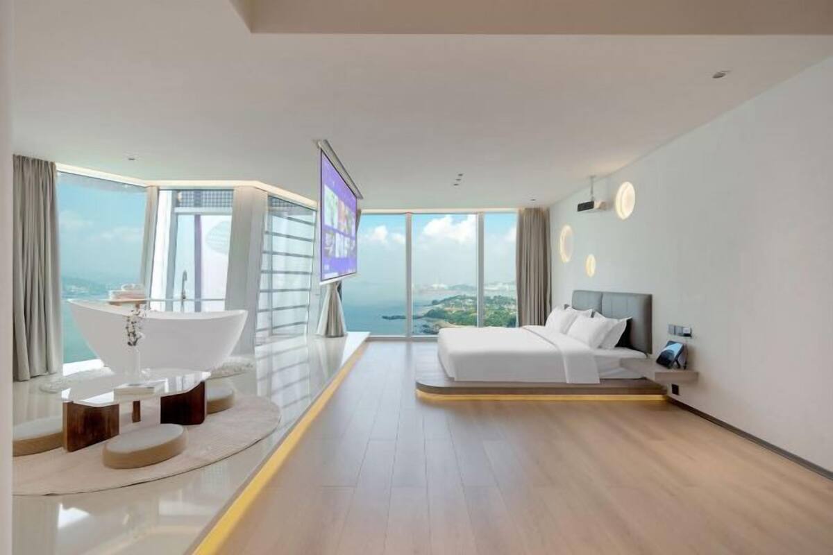 Una habitación de hotel moderna con una cama grande, una bañera y un ventanal con vistas panorámicas.