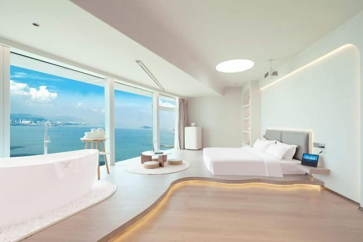 Una habitación de hotel moderna con un ventanal grande, una bañera, una cama y una mesita de noche.