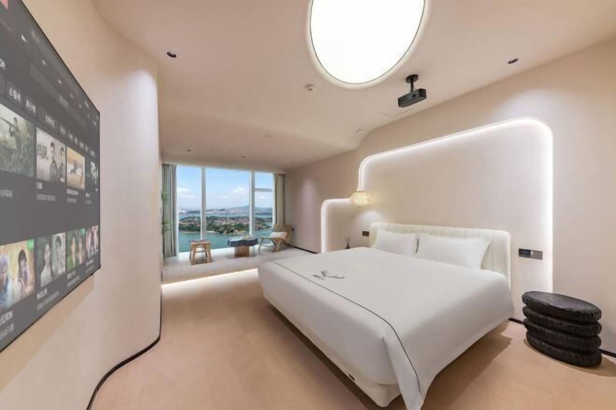 Habitación de hotel moderna con una cama grande, un tragaluz circular, vistas al mar y un televisor montado en la pared.