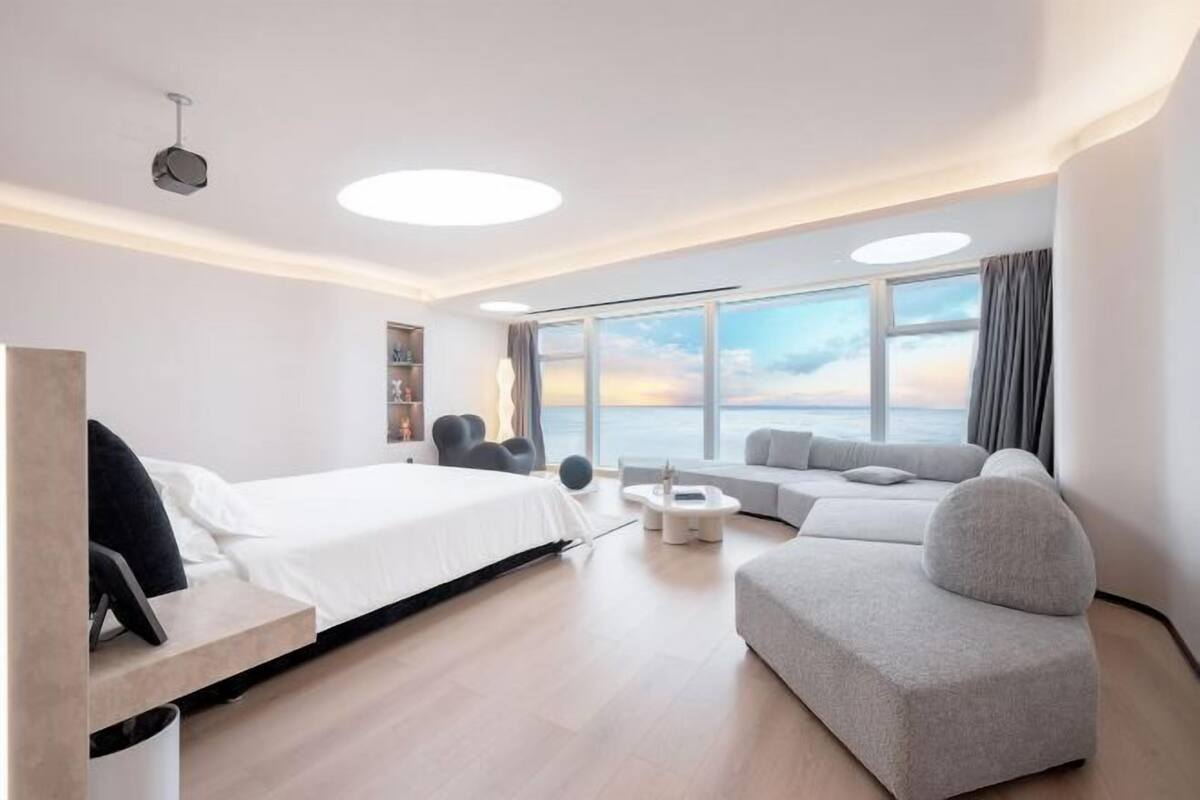 Una habitación de hotel moderna con cama, sofá y vista al mar.