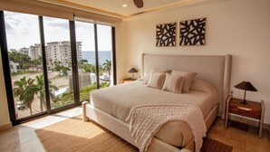A spacious bedroom with a large bed, a ceiling fan, and a view of the ocean through floor-to-ceiling windows. - ATHIMAR Cozumel Condominium w/ Ocean View #406 (Cozumel)