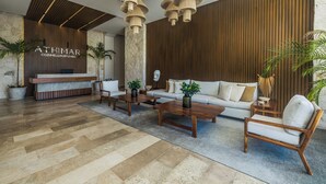 A modern lobby with a reception desk, wooden panel walls, and a seating area with a sofa and chairs. - ATHIMAR Cozumel Condominium w/ Ocean View #406 (Cozumel)