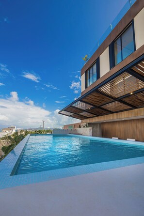 Un edificio moderno con piscina, ventanas amplias y un cielo azul despejado.
