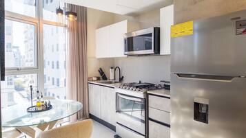 A modern kitchen with a glass dining table, stainless steel appliances, and a view of the city through large windows.