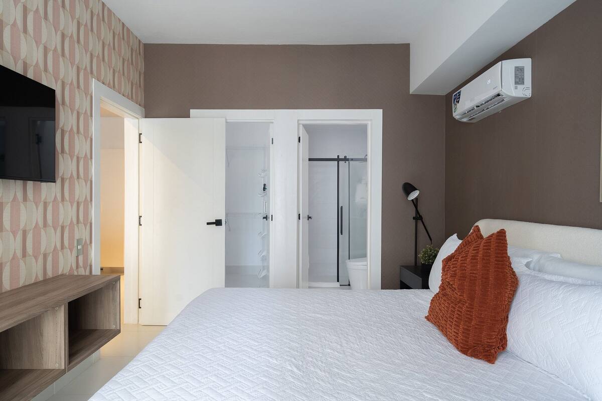 Ein modernes Hotelzimmer mit Bett, Fernseher, Kleiderschrank und Klimaanlage.