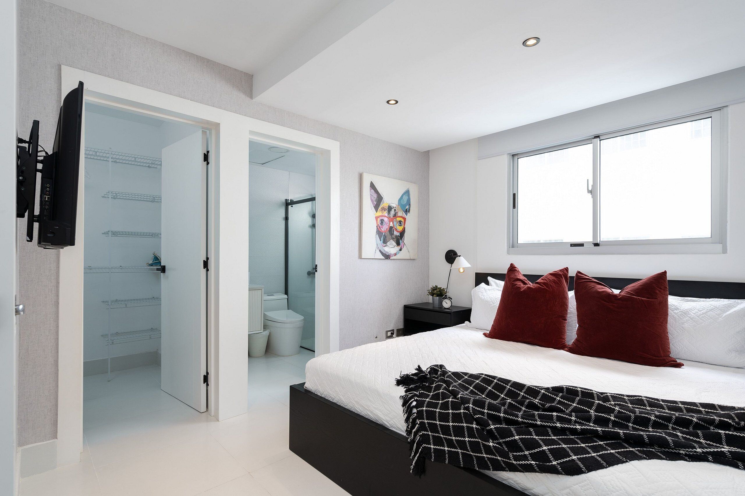 Un dormitorio moderno con una cama grande, una puerta de vidrio que da al baño y un ventanal que proporciona luz natural.