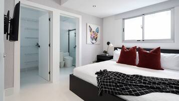 Un dormitorio moderno con una cama grande, una puerta de vidrio que da al baño y un ventanal que proporciona luz natural.