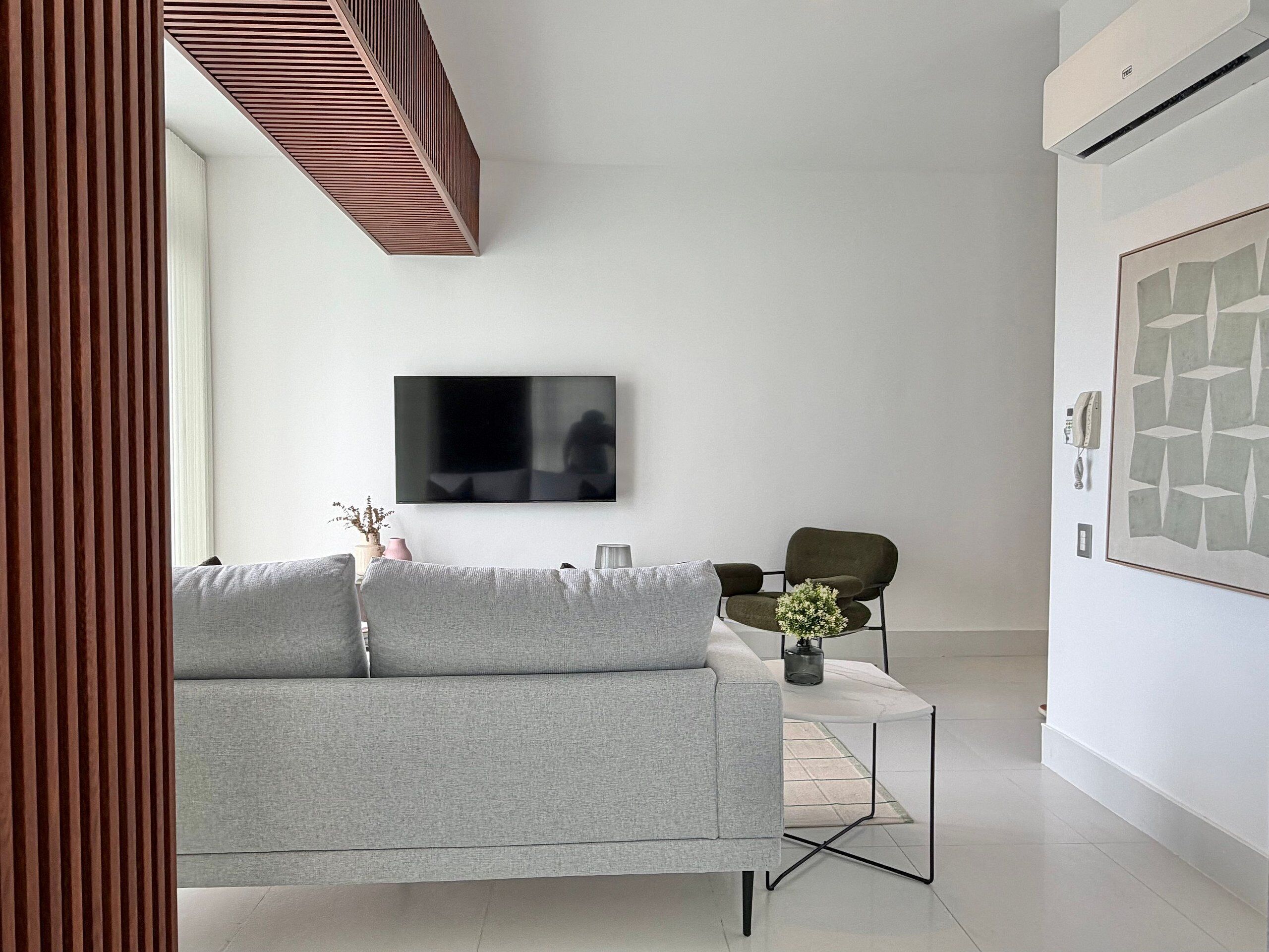 Ein modernes Wohnzimmer mit grauem Sofa, einem Couchtisch, einem an der Wand befestigten Fernseher und einem gerahmten abstrakten Kunstwerk.