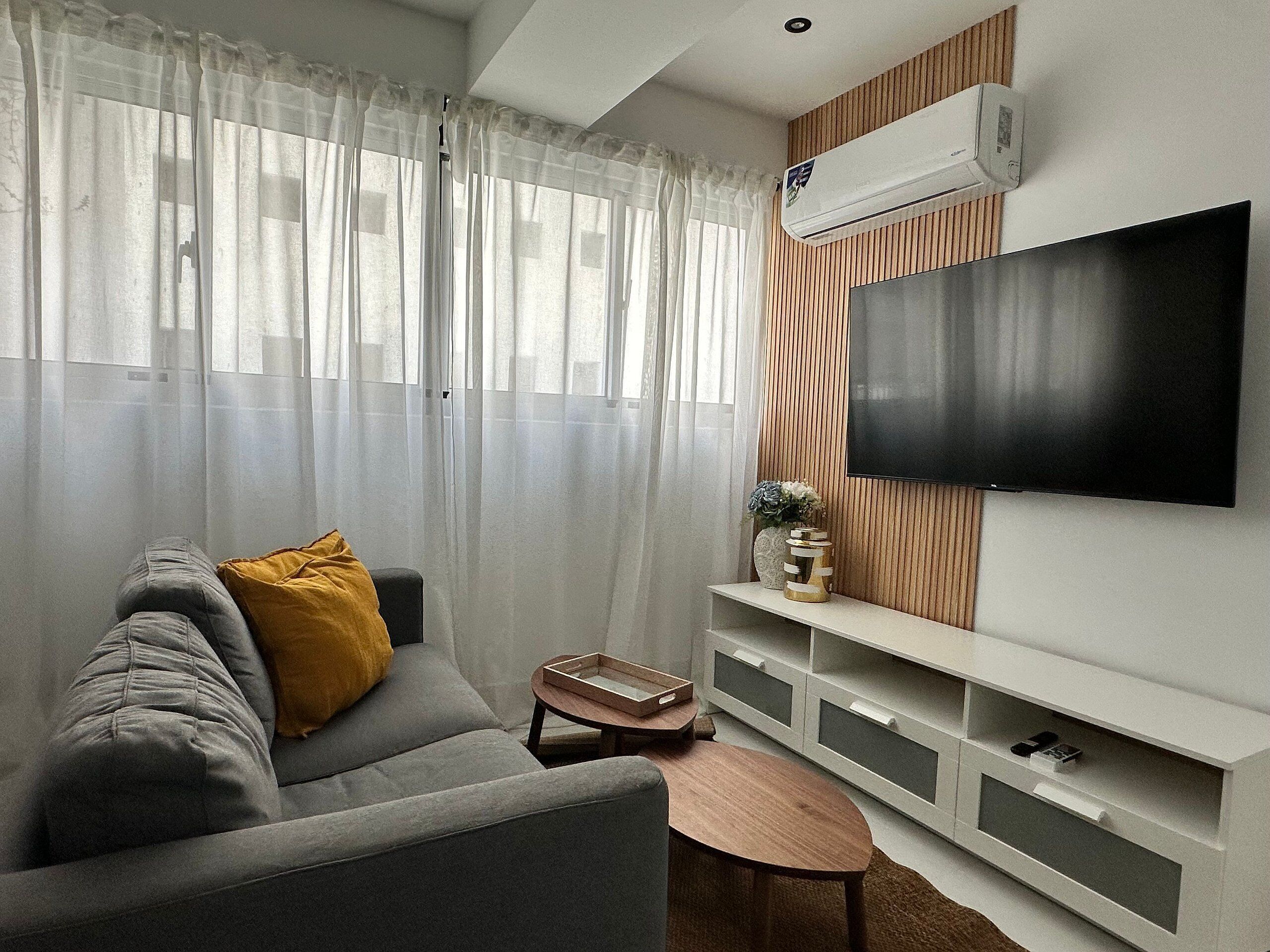 Ein modernes Wohnzimmer mit grauem Sofa, einer Holzkommode, einem Flachbildfernseher und einem kleinen Holztisch.