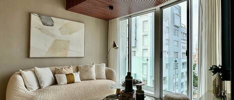 A modern living room with a curved sofa, a round coffee table, and a large window offering a city view.