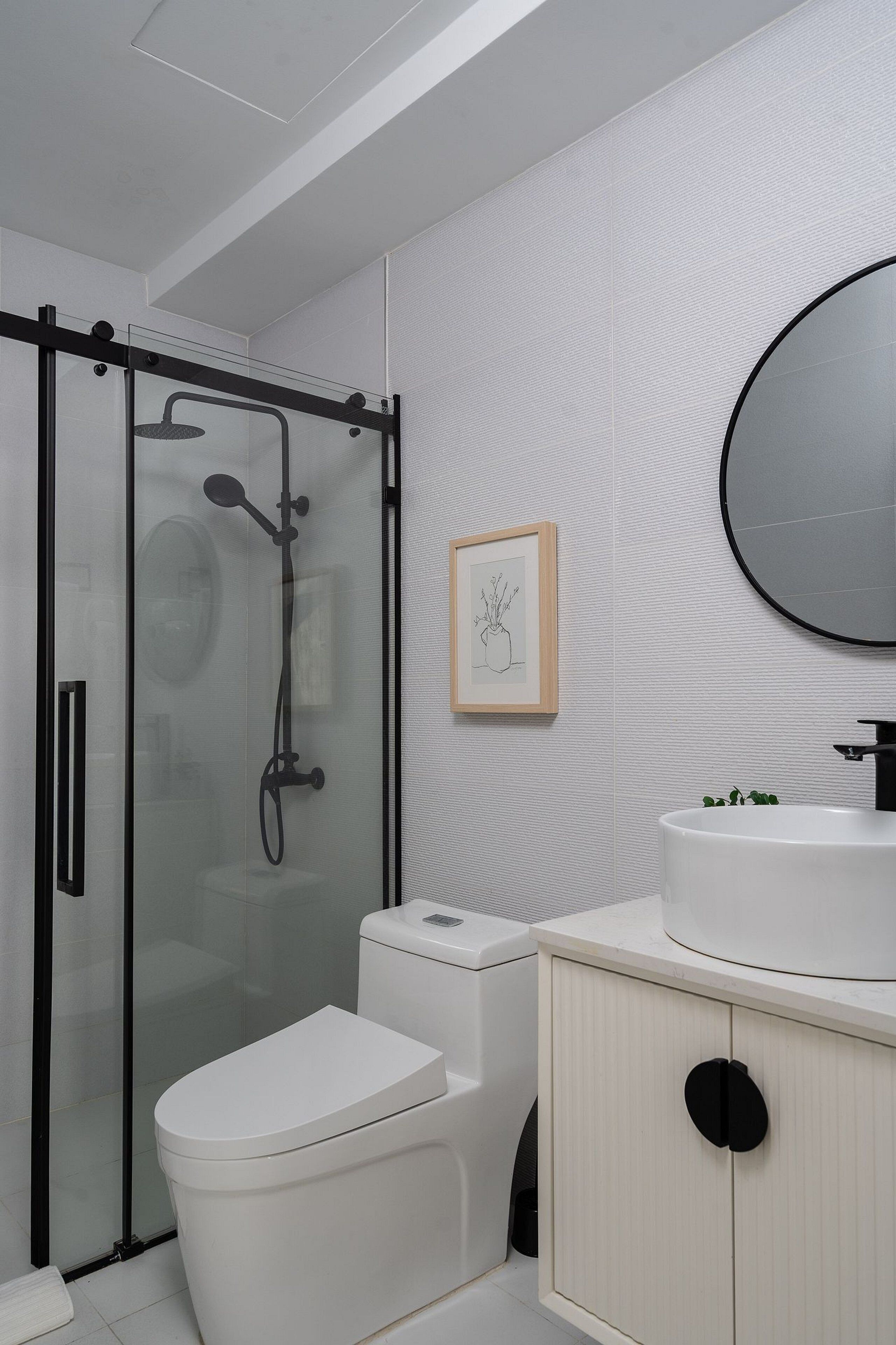 Une salle de bain moderne avec une douche à parois de verre, des toilettes, un lavabo avec un miroir et un tableau encadré au mur.