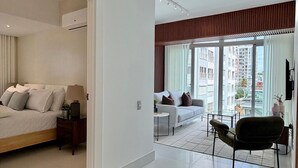 Ett modernt hotellrum med en säng, en soffa, en stol, ett litet bord och en balkong med utsikt över staden.