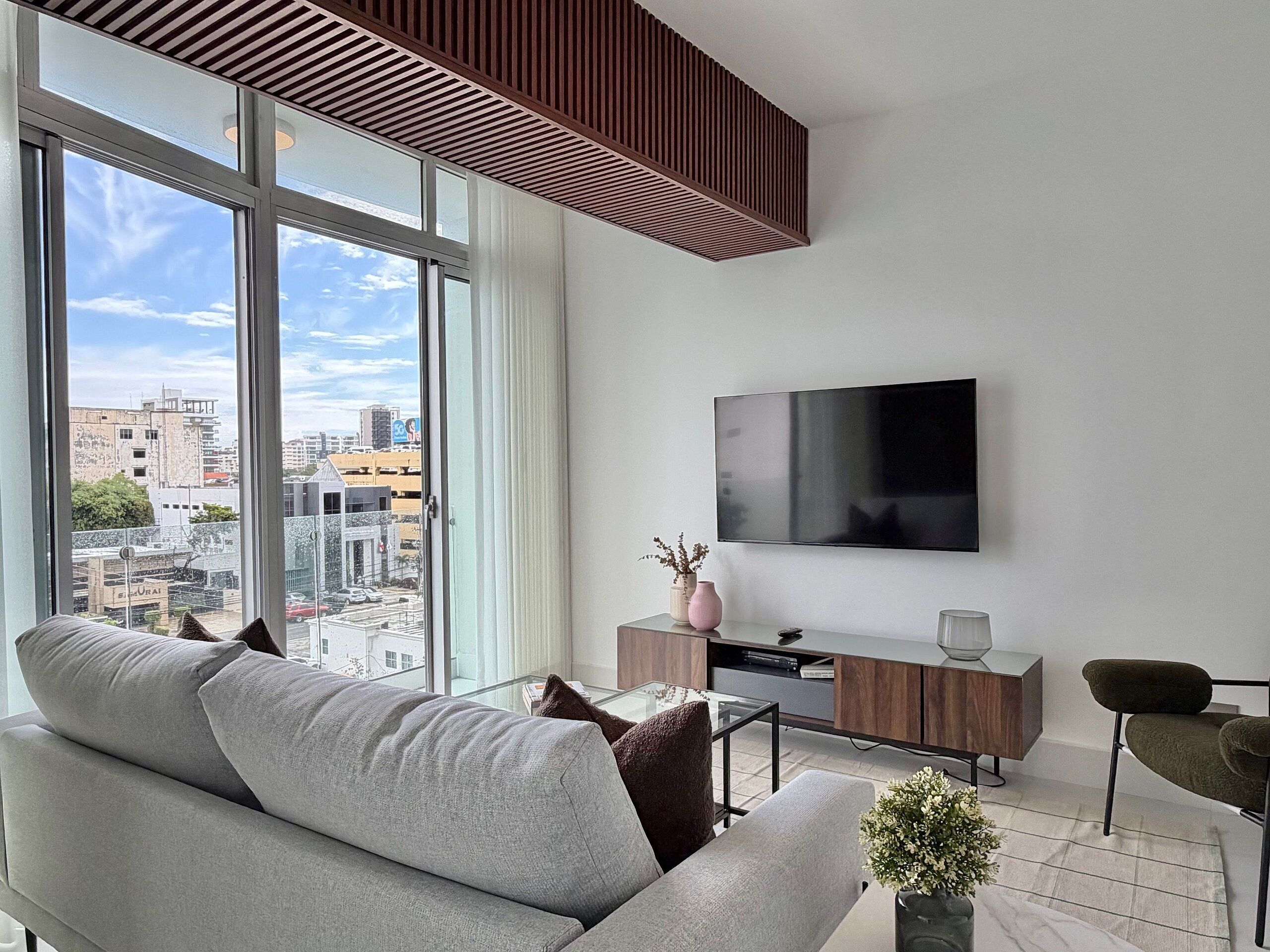 Ein modernes Wohnzimmer mit großem Fenster, Flachbildfernseher, Sofa, Couchtisch und einem kleinen Beistelltisch.