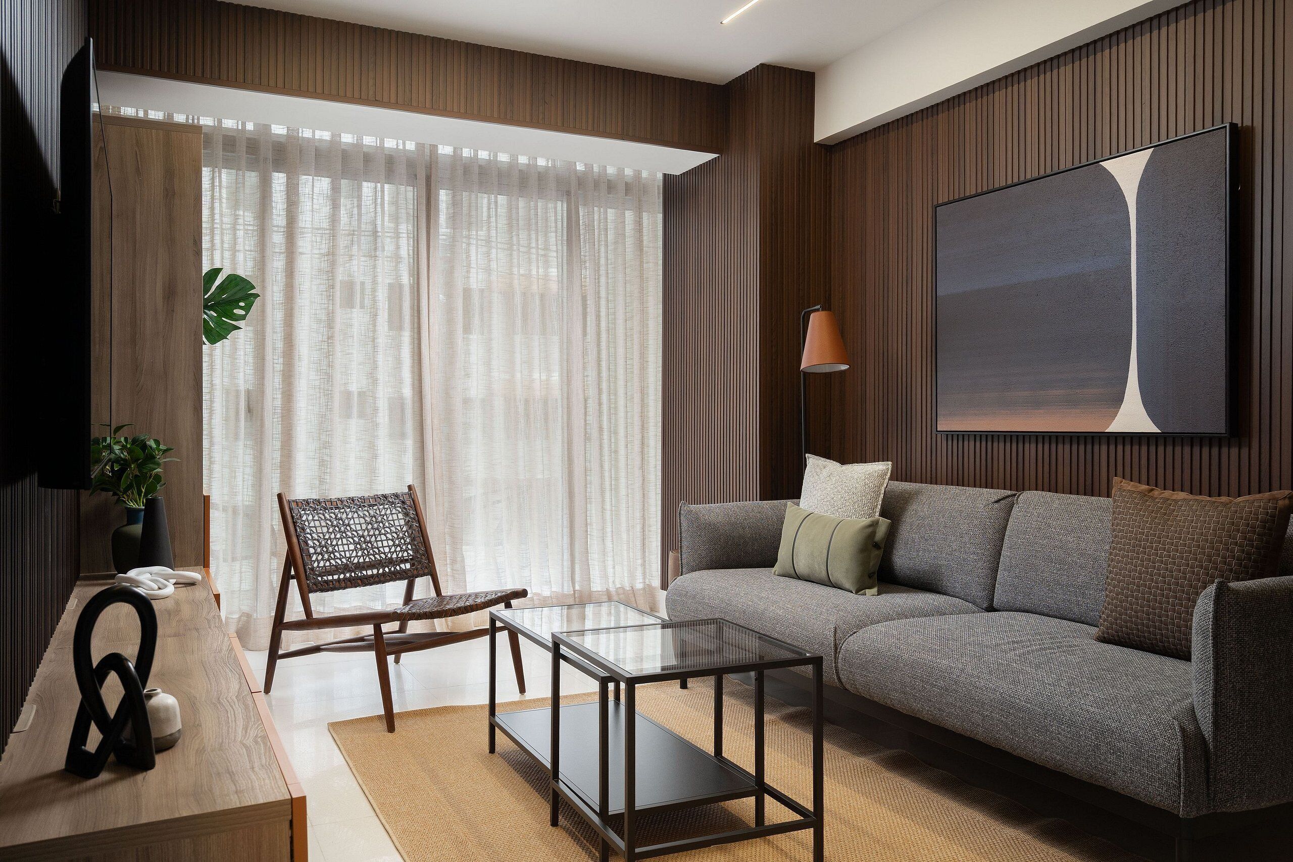 A modern living room with a sofa, a glass coffee table, a wicker chair, a flat-screen TV, and a large abstract painting on the wall.