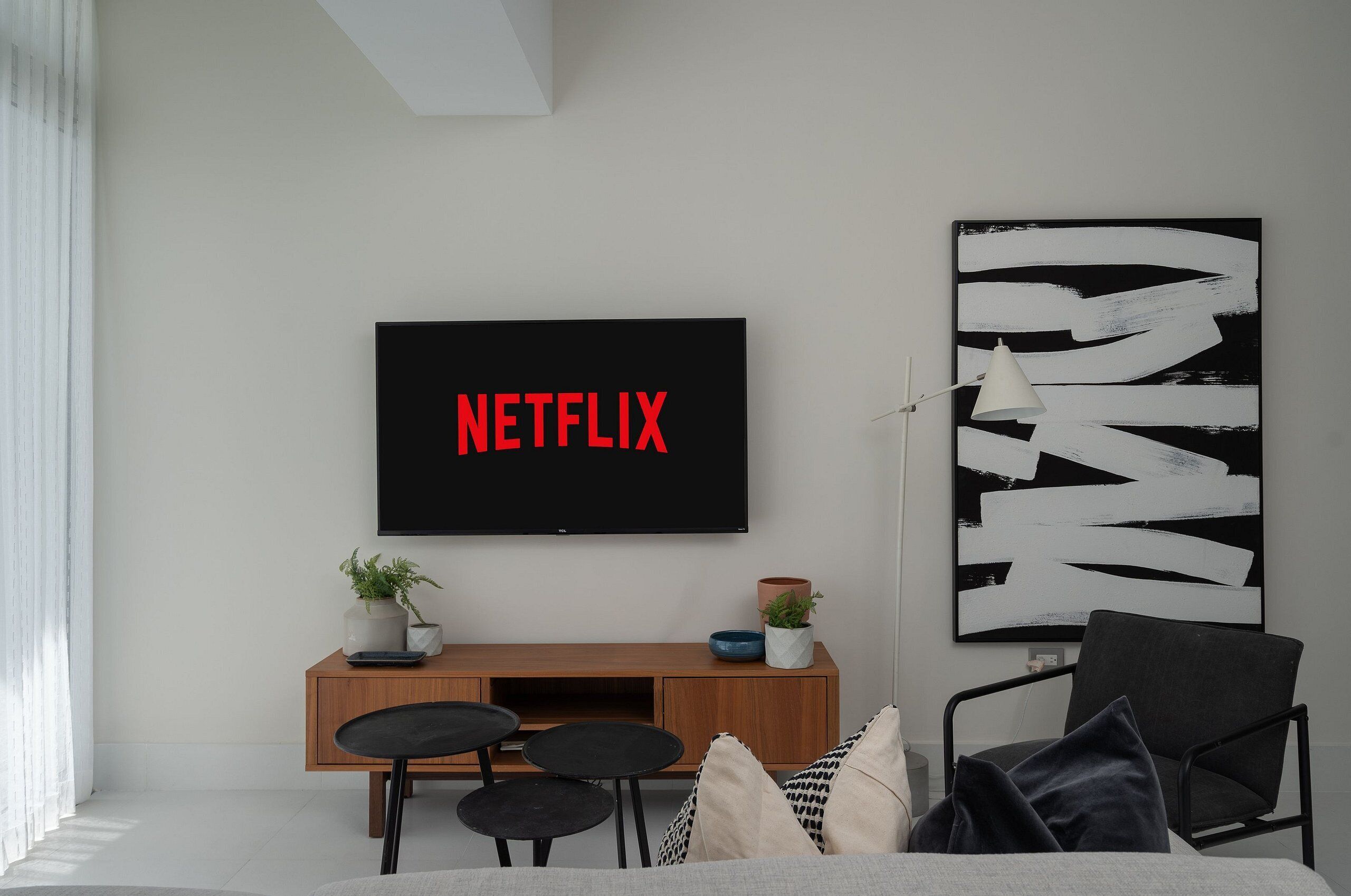 Un salon moderne avec un téléviseur à écran plat fixé au mur, un meuble de rangement en bois en dessous, et un tableau abstrait en noir et blanc accroché au mur.