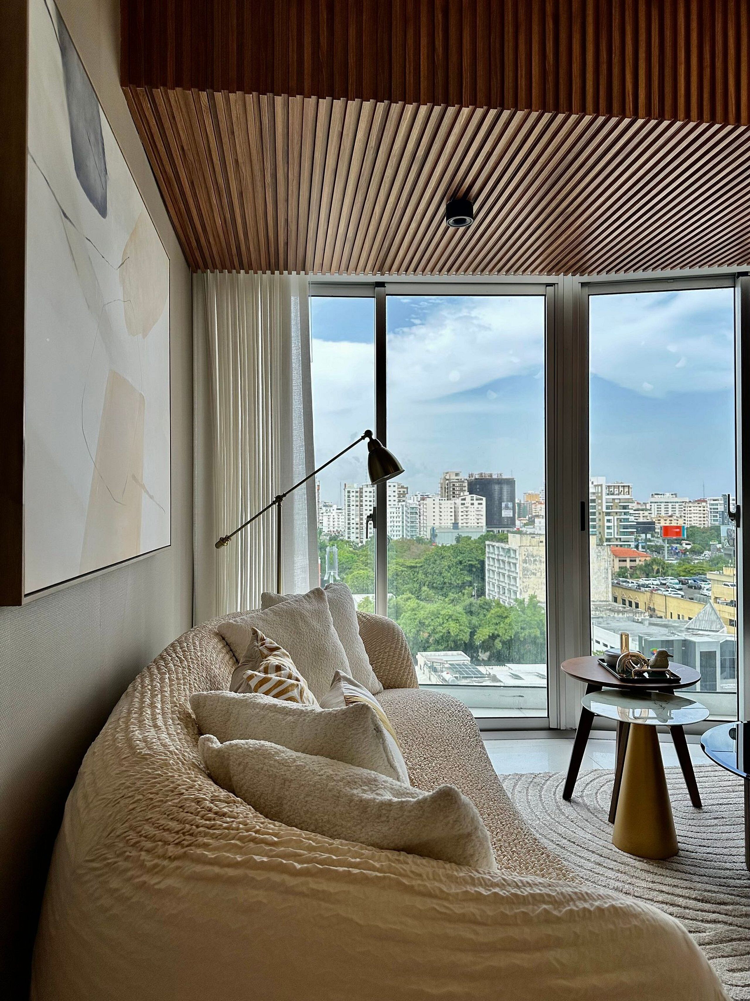 Un dormitorio moderno con una cama grande, una lámpara de pie y vistas a un paisaje urbano a través de amplios ventanales.