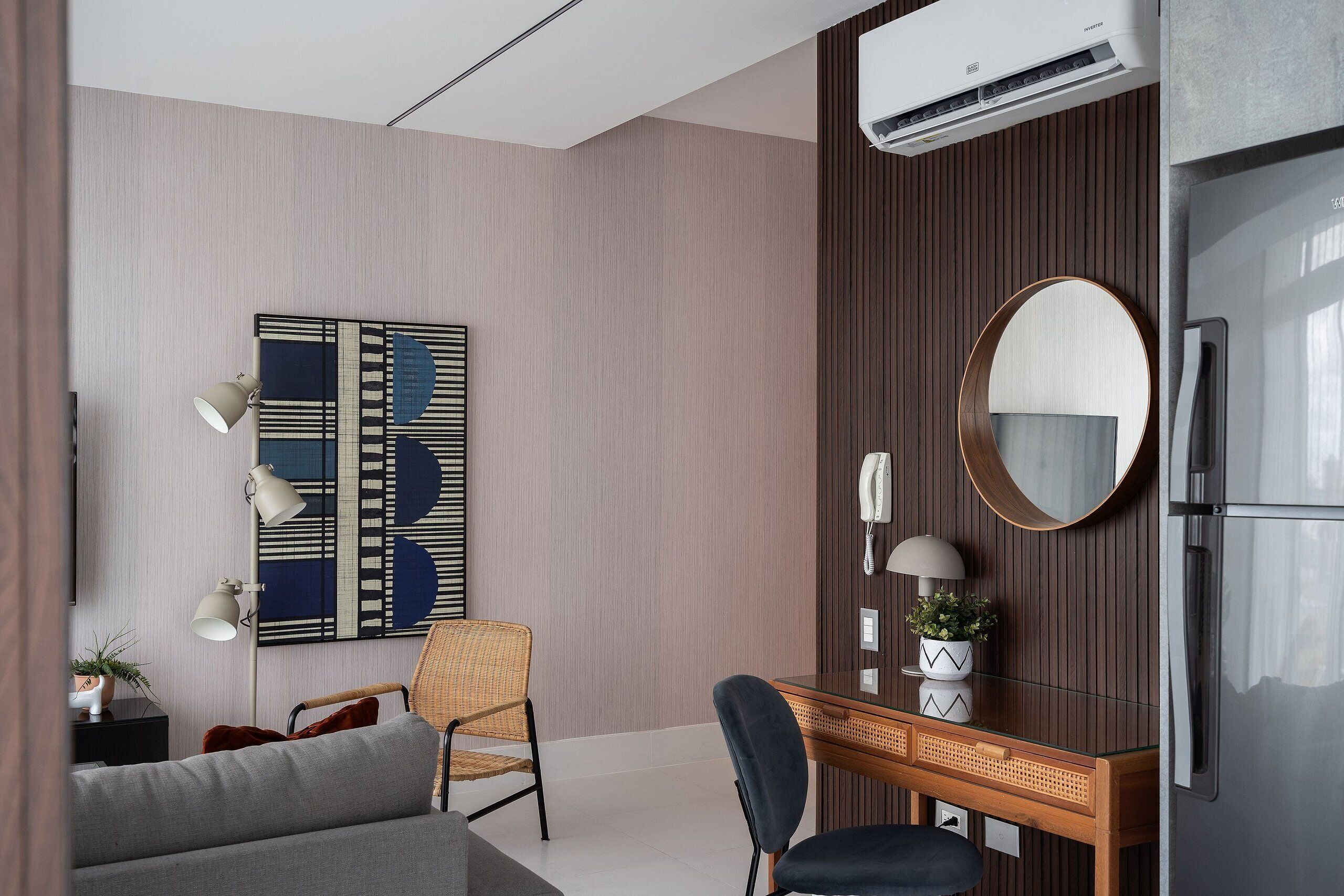 A modern hotel room with a wooden panel wall, a large mirror, a desk with a chair, a sofa, and an air conditioning unit.