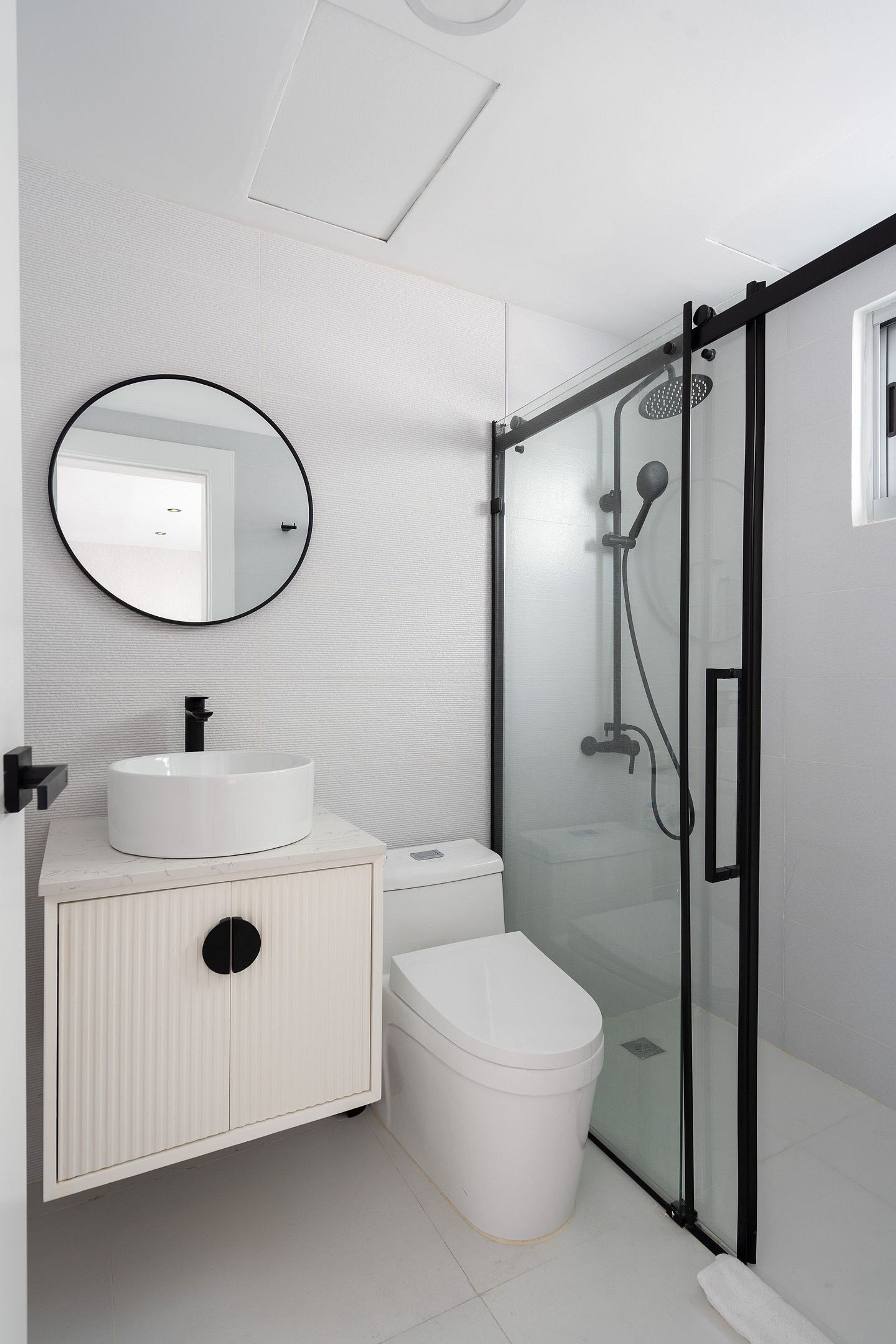 A modern bathroom with a round mirror, white sink, and glass-enclosed shower.