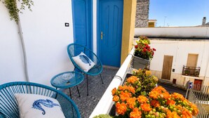 Un balcon avec des portes bleues, deux chaises bleues et un jardinier orné de fleurs oranges.