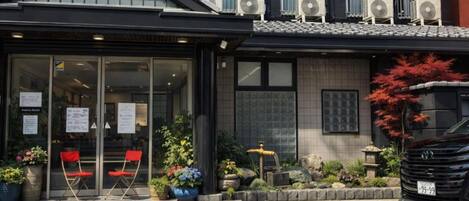 A building with a black facade, large windows, and air conditioning units on the roof. There are two red folding chairs outside, potted plants, and a small fountain.