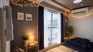 Una habitación acogedora con cama, mesita de noche con lámpara, ventana con cortinas y aire acondicionado instalado en la pared.