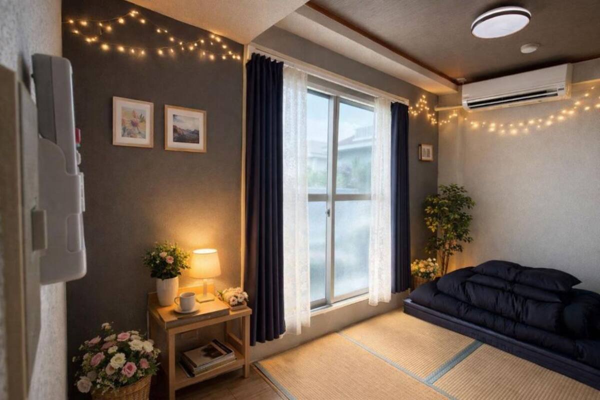 A cozy room with a bed, a bedside table with a lamp, a window with curtains, and a wall-mounted air conditioner.