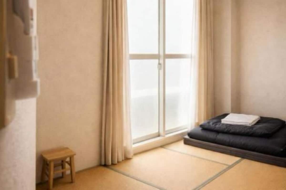 A room with tatami flooring, a sliding door, a small wooden stool, and a black sofa with cushions.