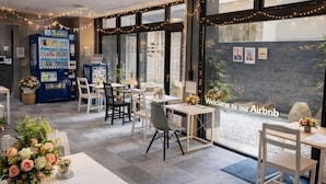 Un comedor interior con mesas y sillas, una máquina expendedora y un letrero de bienvenida.