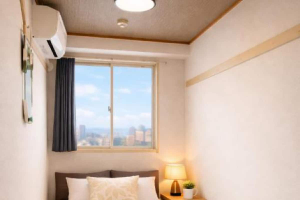 A neatly made bed with a pillow, a bedside lamp, and a window with a view of the city.