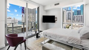 A modern hotel room with a bed, a TV, a chair, and a balcony with a city view. - Your Terrace Your Bay Your Moment Pool Gym (Miami)