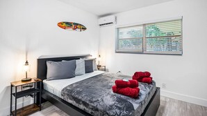 Una camera da letto moderna con un letto, comodini, condizionatore d'aria a parete e una finestra con tende.